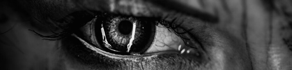 Alt text: "Black and white close-up of an eye, expressing pain, anger, and fear, representing the 'Dark Night of the Soul' and the dissolution of the false self.